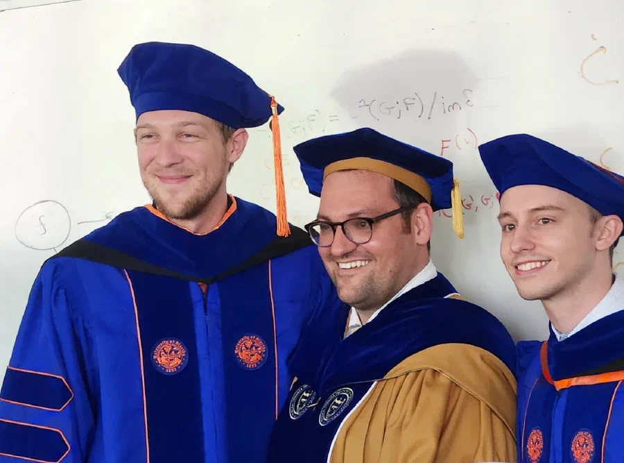 Tyler Hanks, James Fairbanks and Luke Morris, May 2026 — the whiteboard behind them still carries the sheaf cohomology from the week before.