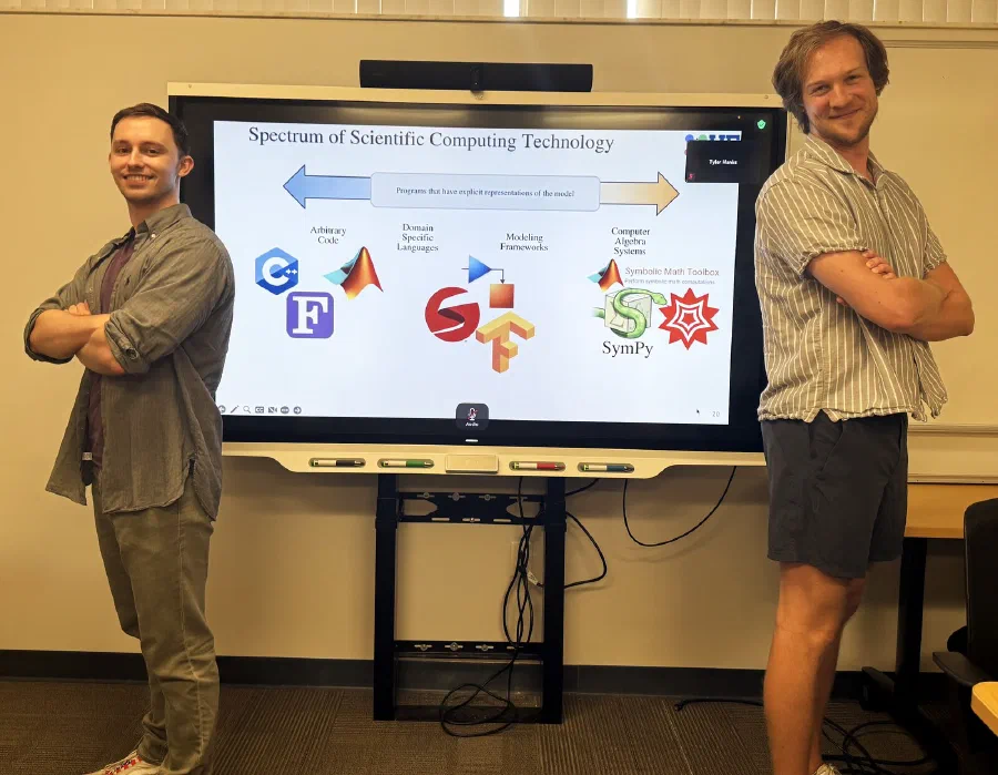 Luke Morris and Tyler Hanks in the lab, April 2026, in front of the spectrum of scientific computing technology.